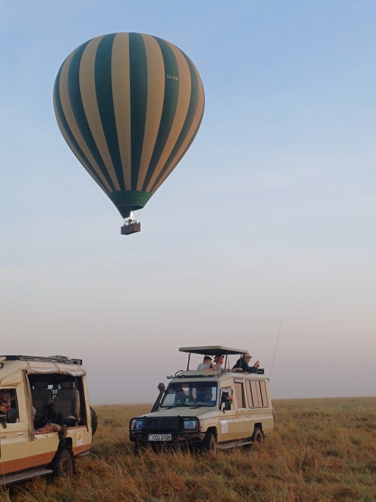 A hot air balloon rising over the savanna beside two Mzingo safari vehicles
